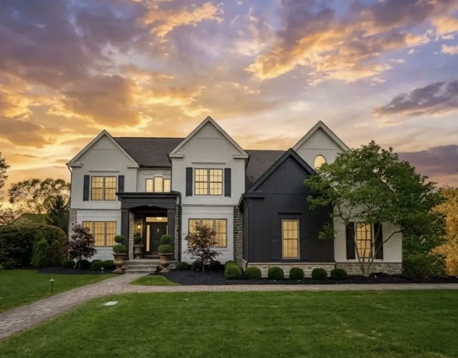 The farmhouse exterior at sunset, white and black siding with glowing windows