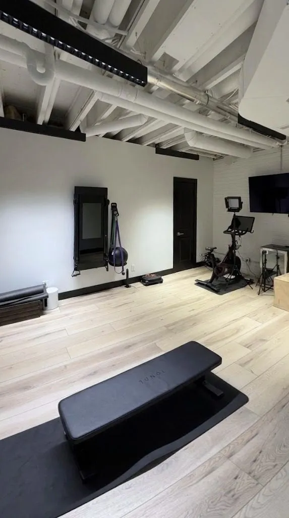Open home gym with light wood floors, a bench and a bike